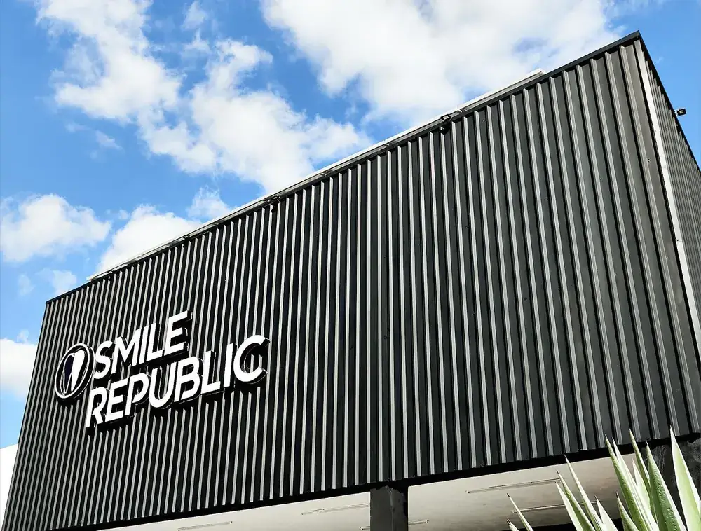 Fachada de Smile Republic Las Américas, con su letrero blanco sobre muro negro y cielo azul