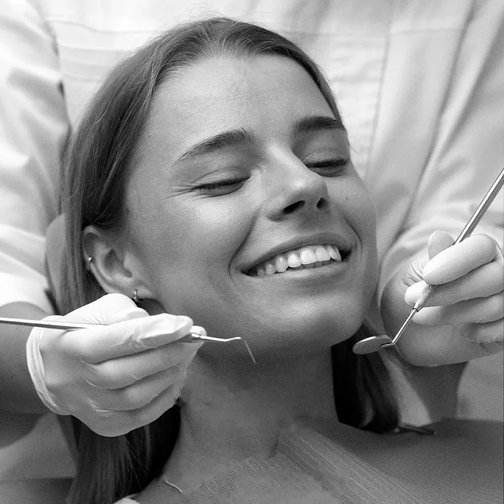Mujer sonriendo con los ojos cerrados durante una revisión dental, en blanco y negro