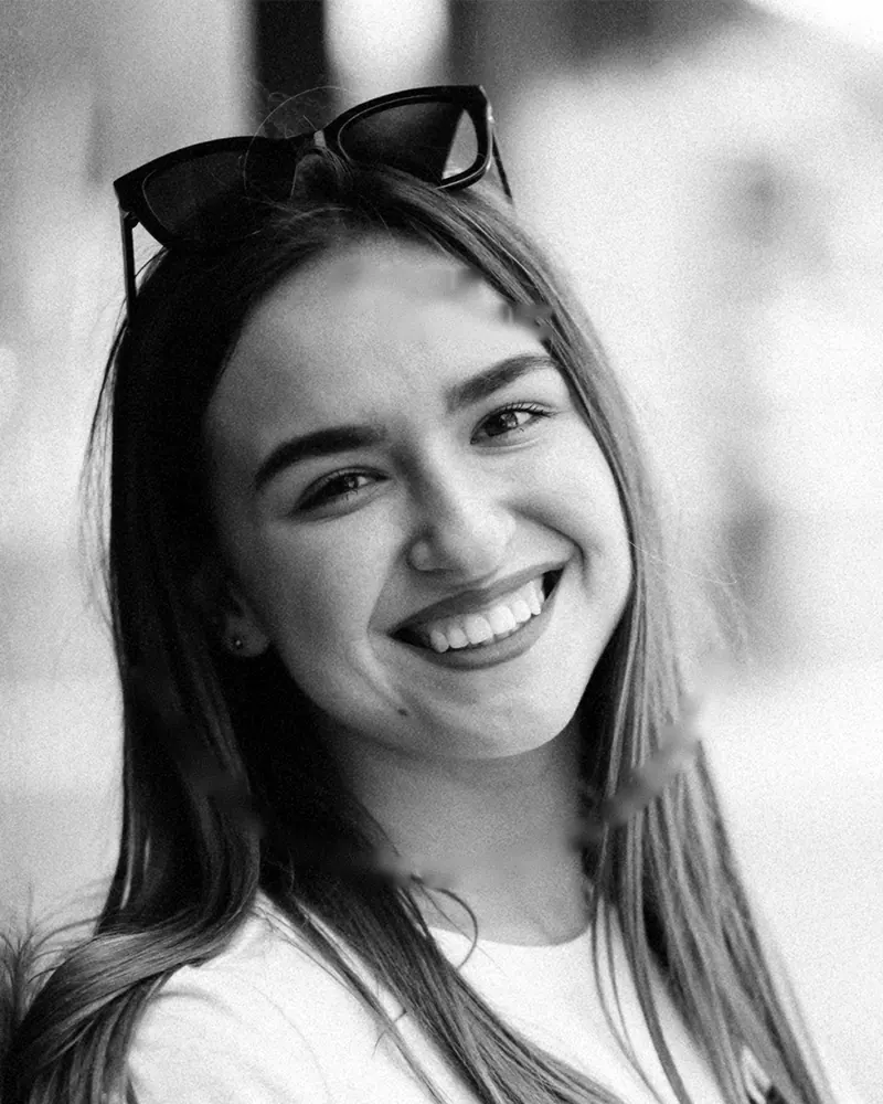 Joven sonriendo con lentes de sol sobre la cabeza, en blanco y negro