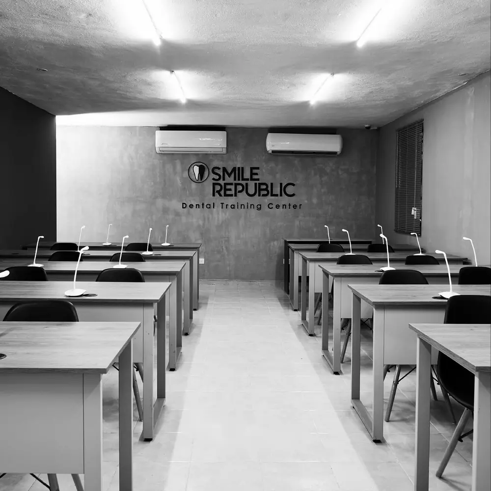 Aula de Smile Republic Dental Training Center con mesas, lámparas y el logo en un muro de concreto