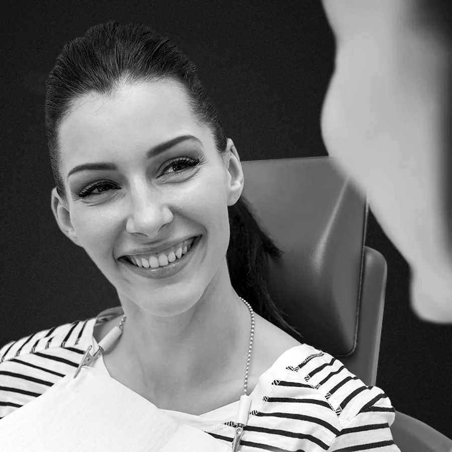 Paciente sonriendo en el sillón dental durante una consulta, en blanco y negro